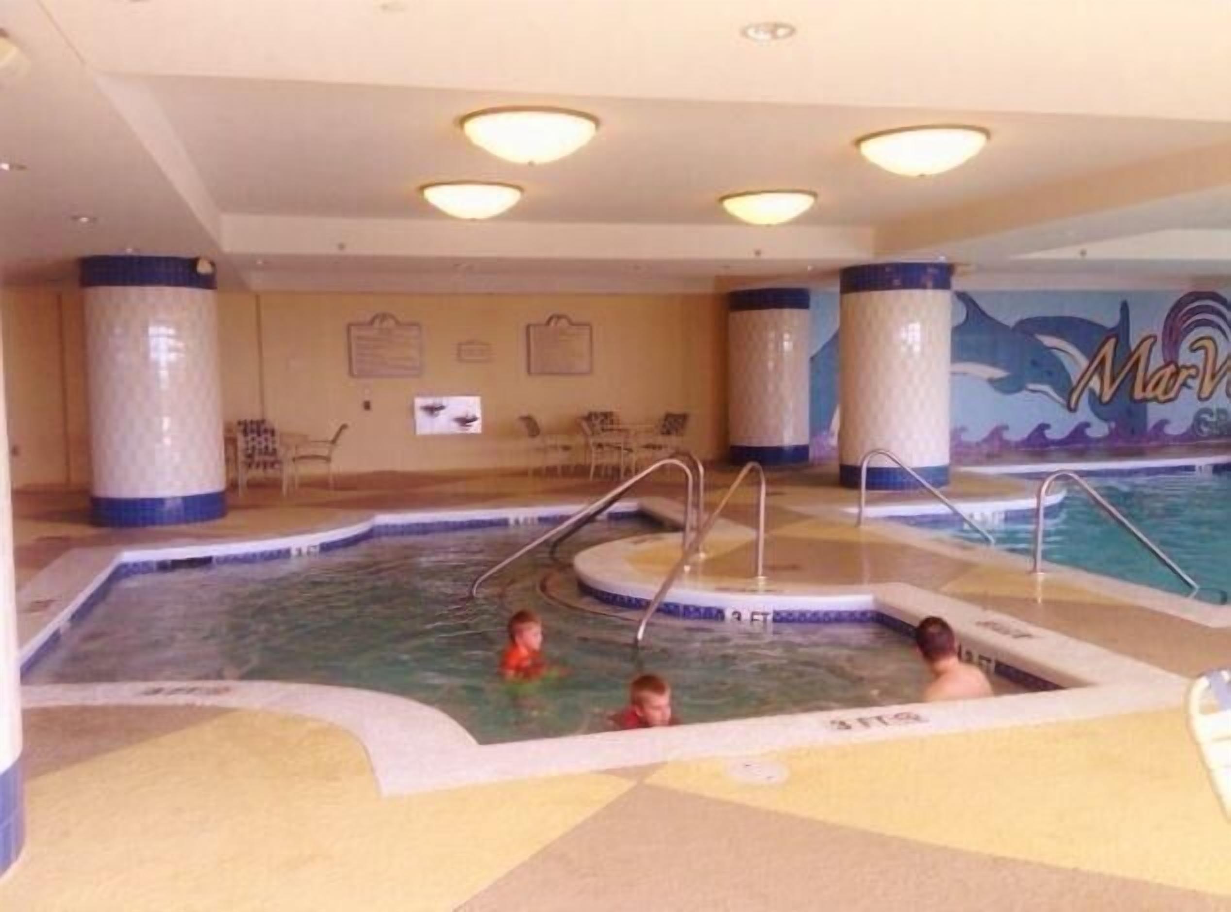An indoor swimming pool with multiple lanes, a mural on the wall, and a seating area with chairs.