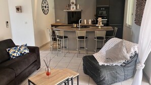 Un soggiorno moderno con un divano, un tavolino da caffè e un poggiapiedi nero. C'è un angolo cottura con un bancone e delle sedie.