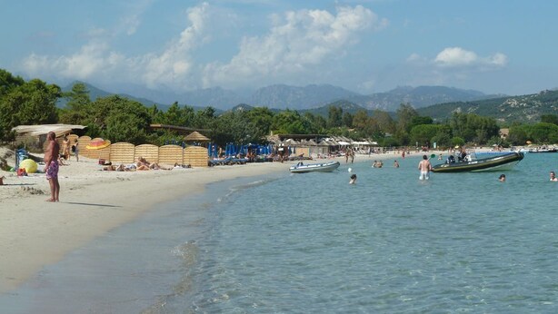 Una spiaggia con acque cristalline, ombrelloni e barche.
