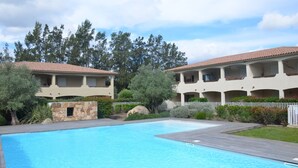 Una piscina con bordo in legno, circondata da un recinto bianco, adiacente a un edificio con balconi.
