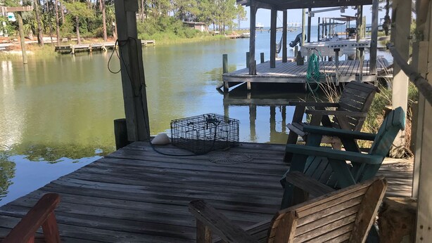A wooden dock with chairs and a table, overlooking a calm lake with trees in the background. - Perfect Couples Getaway - Canal Front Apartment  (Eastpoint)