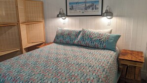 A bedroom with a bed, a wooden nightstand, a wall-mounted lamp, a framed picture, and a woven headboard. - Perfect Couples Getaway - Canal Front Apartment  (Eastpoint)