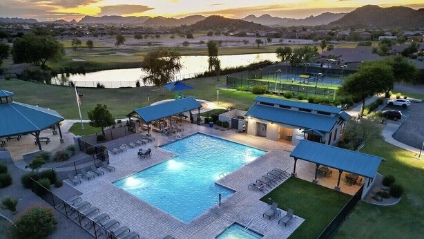 A swimming pool with lounge chairs and a covered patio area, surrounded by a landscaped garden and a view of a lake and mountains. - Luxurious Golf Course Views-Private Pool +2 King Suites-Sleeps 8 (San Tan Valley)