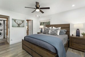 Un dormitorio con cama, ventilador de techo, mesita de noche, lámpara y televisor montado en la pared.
