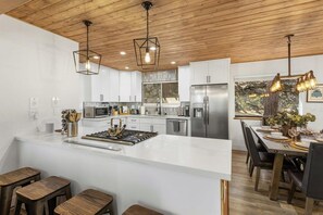 A modern kitchen with white cabinetry, a central island, and a dining area with a wooden table and chairs.