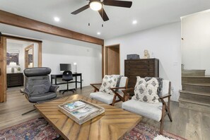 A living room with a wooden coffee table, two armchairs, a leather chair, a television, and a staircase.