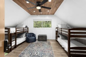 Een slaapkamer met twee stapelbedden, een plafondventilator, een raam en een kamerkleed met patroon.