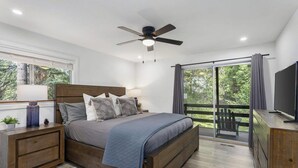 Une chambre à coucher comprenant un lit, des tables de chevet, un téléviseur et un balcon avec vue sur les arbres.