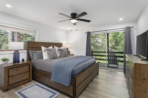 Een slaapkamer met een bed, nachtkastjes, een televisie en een balkon met uitzicht op bomen.