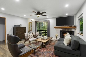 A living room with a fireplace, a television, and a ceiling fan.