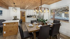 Une cuisine moderne avec des meubles blancs, un îlot central en bois et un coin repas avec une table en bois, dressée pour quatre personnes.