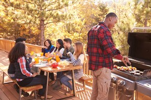 Een groep mensen dineert buiten op een houten terras met een barbecue.