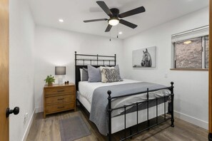 A bedroom with a bed, a nightstand, a lamp, a ceiling fan, and a window with a view.