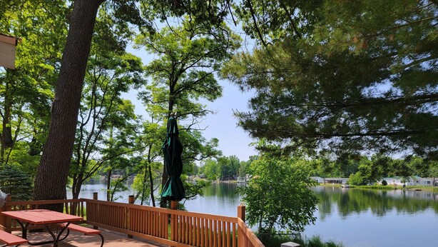 A wooden deck with picnic tables overlooking a calm lake, surrounded by trees. - LAKEFRONT COTTAGE  (Lake George)