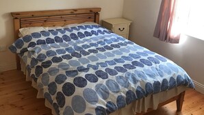 Un lit avec une couvre-lit à pois bleus et blancs, une tête de lit en bois et une table de chevet avec un tiroir.
