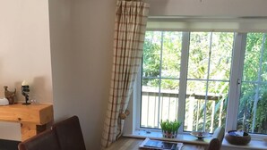 Un coin repas comprenant une table en bois, quatre chaises, une fenêtre donnant sur un paysage verdoyant et un rideau.