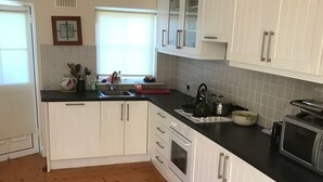 Une cuisine avec des meubles blancs, un plan de travail noir et un plancher en bois.