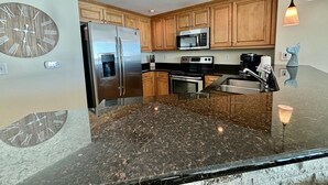A modern kitchen with wooden cabinets, stainless steel appliances, granite countertops, pendant lighting, and a decorative clock. - MVG 1112 3 Bedroom 3 Bath Oceanfront (North Myrtle Beach)