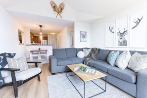 Una sala de estar moderna con un sofá gris, una mesa de centro de madera y una zona de comedor con una mesa y sillas blancas.