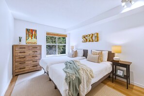 Un dormitorio con dos camas, un aparador de madera, una ventana con persianas y una lámpara de pared.