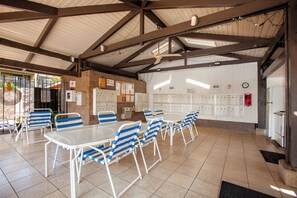 A covered dining area with tables and chairs, a wall with lockers, and a ceiling fan.