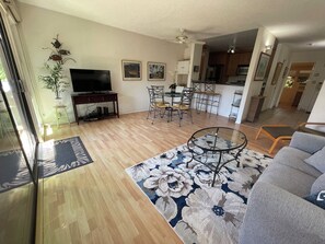 A spacious living room with a flat-screen TV, a dining area with a table and chairs, and a kitchen in the background.