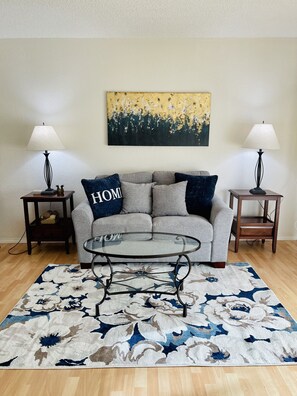 A living room with a grey sofa, two side tables with lamps, a glass coffee table, and a floral rug.