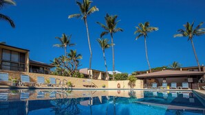 Una piscina con sillones de descanso, palmeras y edificios de hotel al fondo.