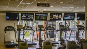 Ein Fitnessraum mit mehreren Laufbändern und Trainingsgeräten, einem Schild für Handtücher und Fernsehern, die verschiedene Sender zeigen.