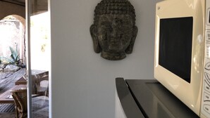 A room with a Buddha statue on the wall, a microwave, and a door leading to an outdoor area with a wooden deck. - Mas des Micocouliers (Montagnac)