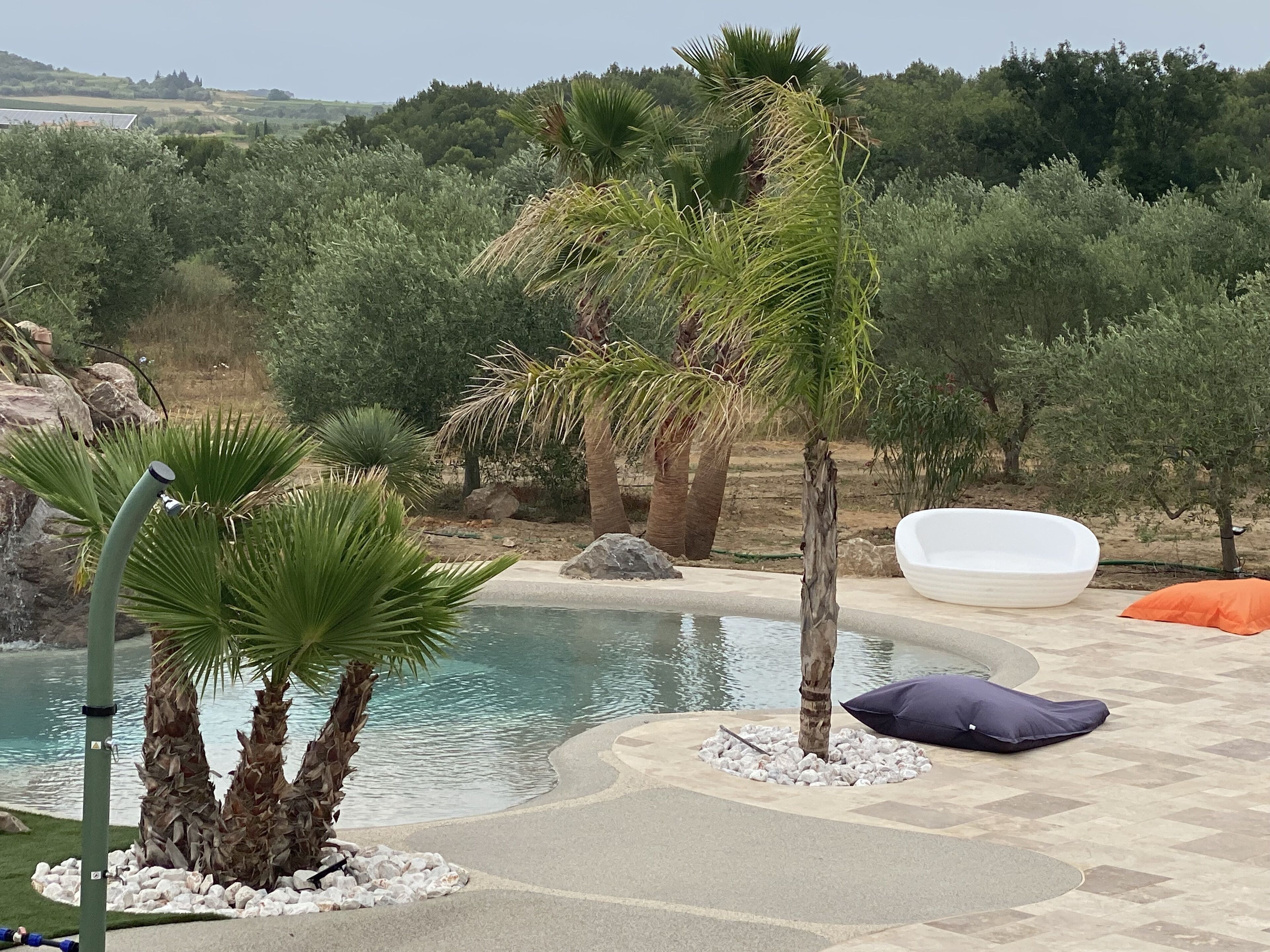 A pool area with palm trees, a white lounge chair, and a pebble bed.