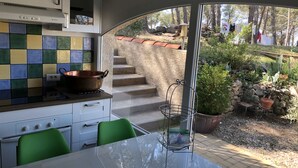 A kitchen with a tiled backsplash, a stove, and a window overlooking a garden with steps and plants. - Mas des Micocouliers (Montagnac)