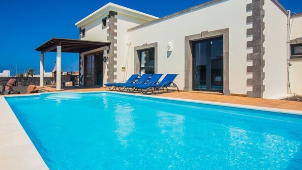 A modern building with a swimming pool, blue lounge chairs, and a covered patio area. - Villa Eleonor in Playa Blanca (Playa Blanca)