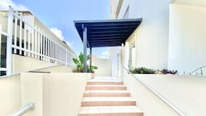 Una escalera conduce a un área cubierta, con barandilla de metal a un lado y cerca blanca al otro.