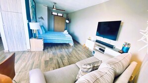 Una habitación de hotel moderna con sofá, cama con ropa de cama a rayas, televisor de pantalla plana y ventilador de techo.