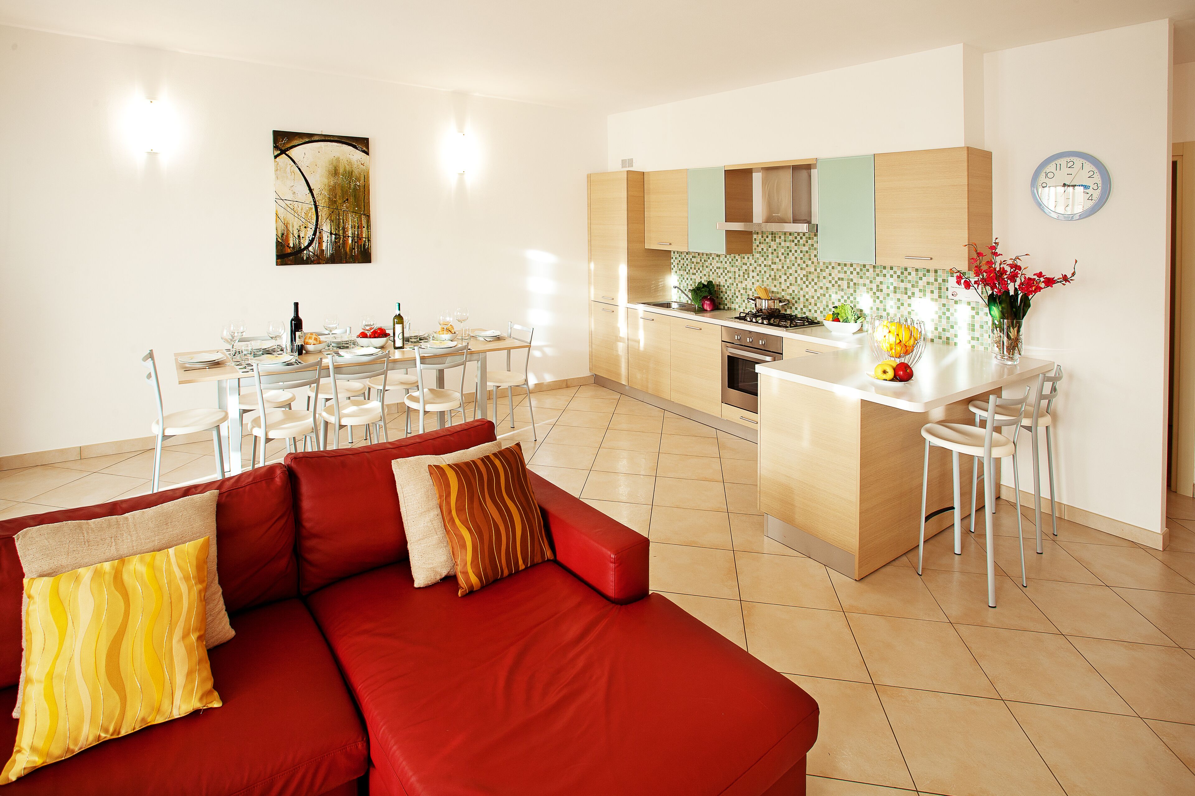 Une cuisine moderne avec un coin repas, comprenant un canapé rouge, des chaises blanches et un mur recouvert de carreaux.