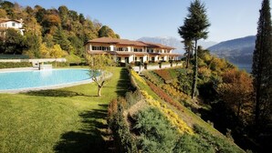 Un grand immeuble à étages, doté d’une piscine, entouré de jardins en terrasses et surplombant un paysage montagneux.