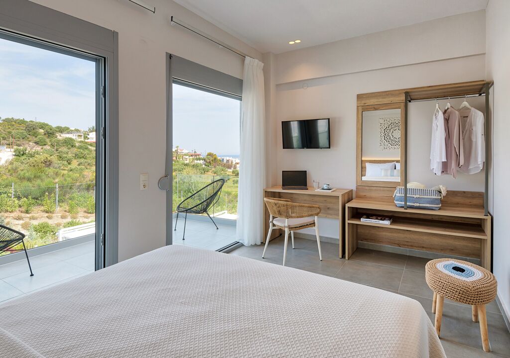 Une chambre moderne avec un grand lit, un bureau avec un ordinateur, une télévision et une vue sur la verdure.