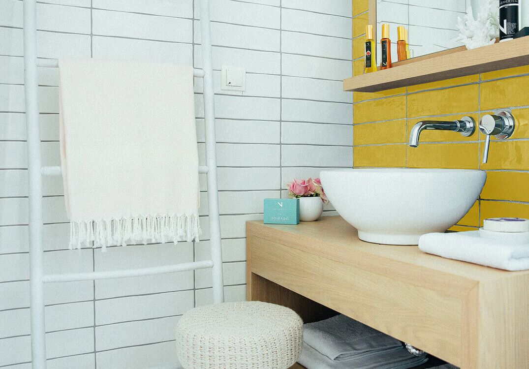 A bathroom with white tiled walls, a wooden vanity, a white sink, and a towel rack.