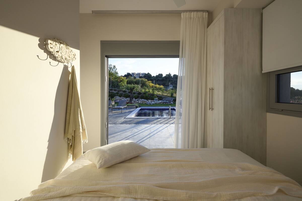 Ein Schlafzimmer mit Bett, Blick auf einen Swimmingpool und einem Balkon.