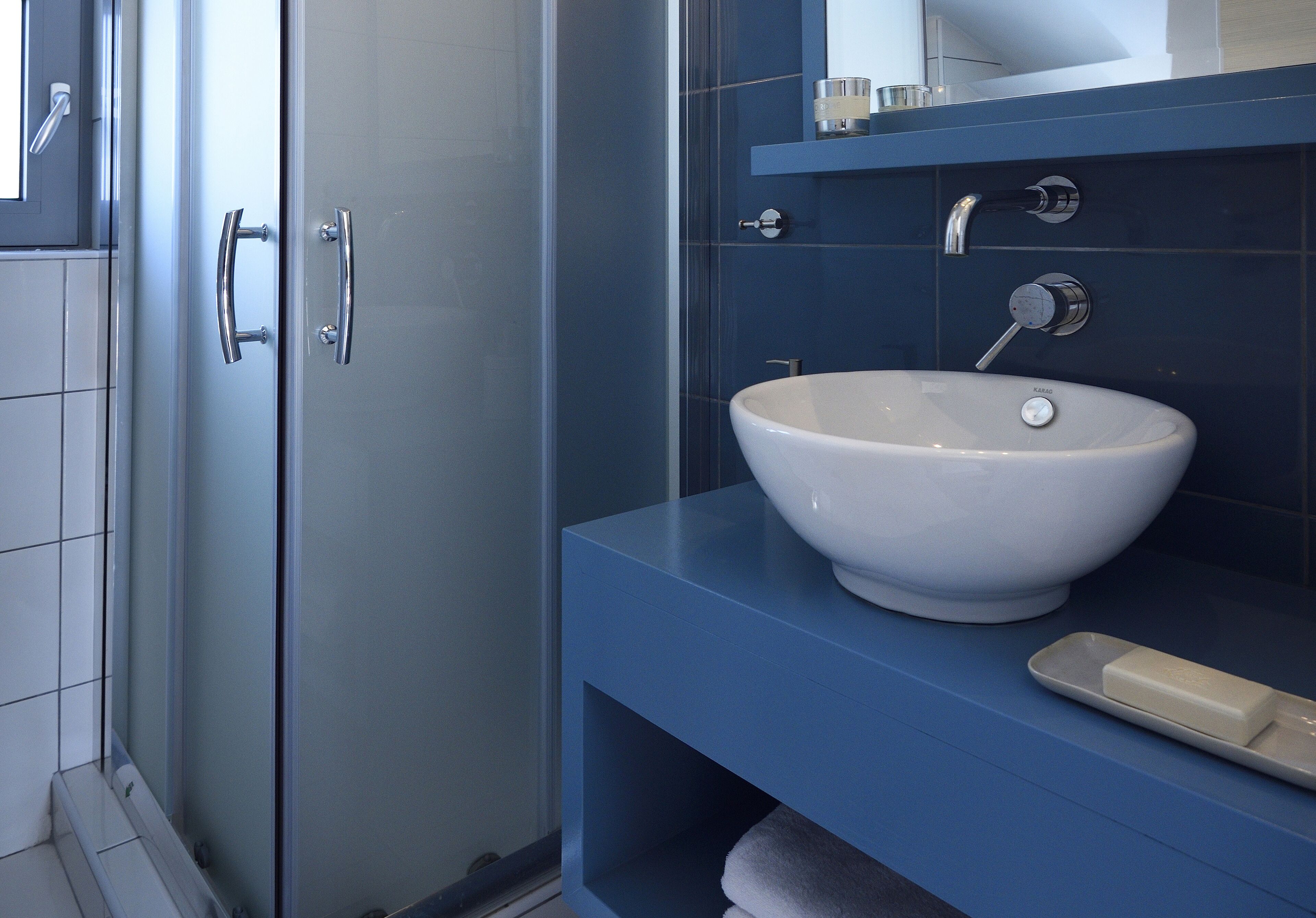 A bathroom with a white sink, a blue vanity, and a glass shower enclosure.