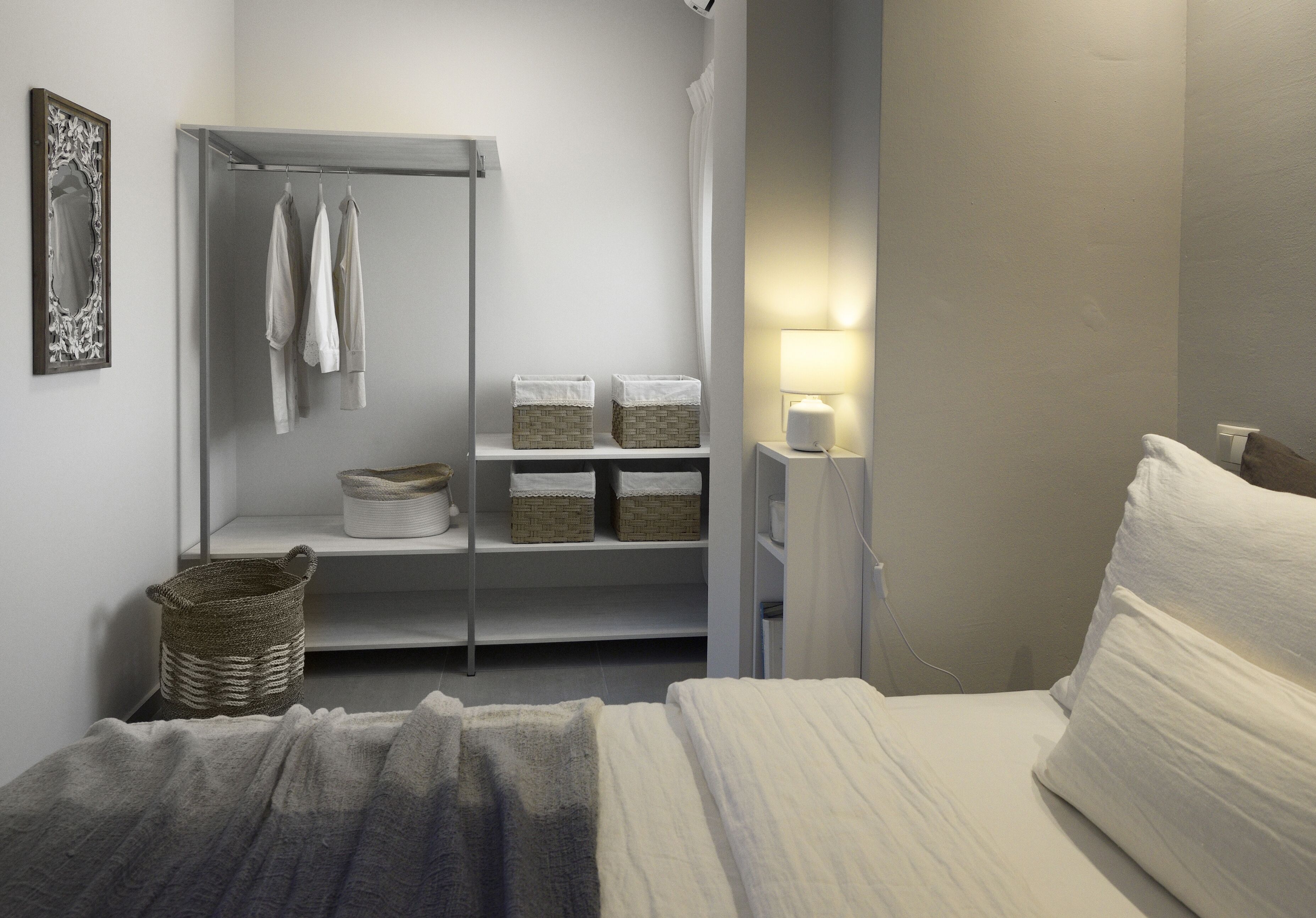 Un dormitorio con cama, armario, estante con cestas y lámpara de noche.