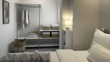 A bedroom with a bed, a wardrobe, a shelf with baskets, and a bedside lamp.