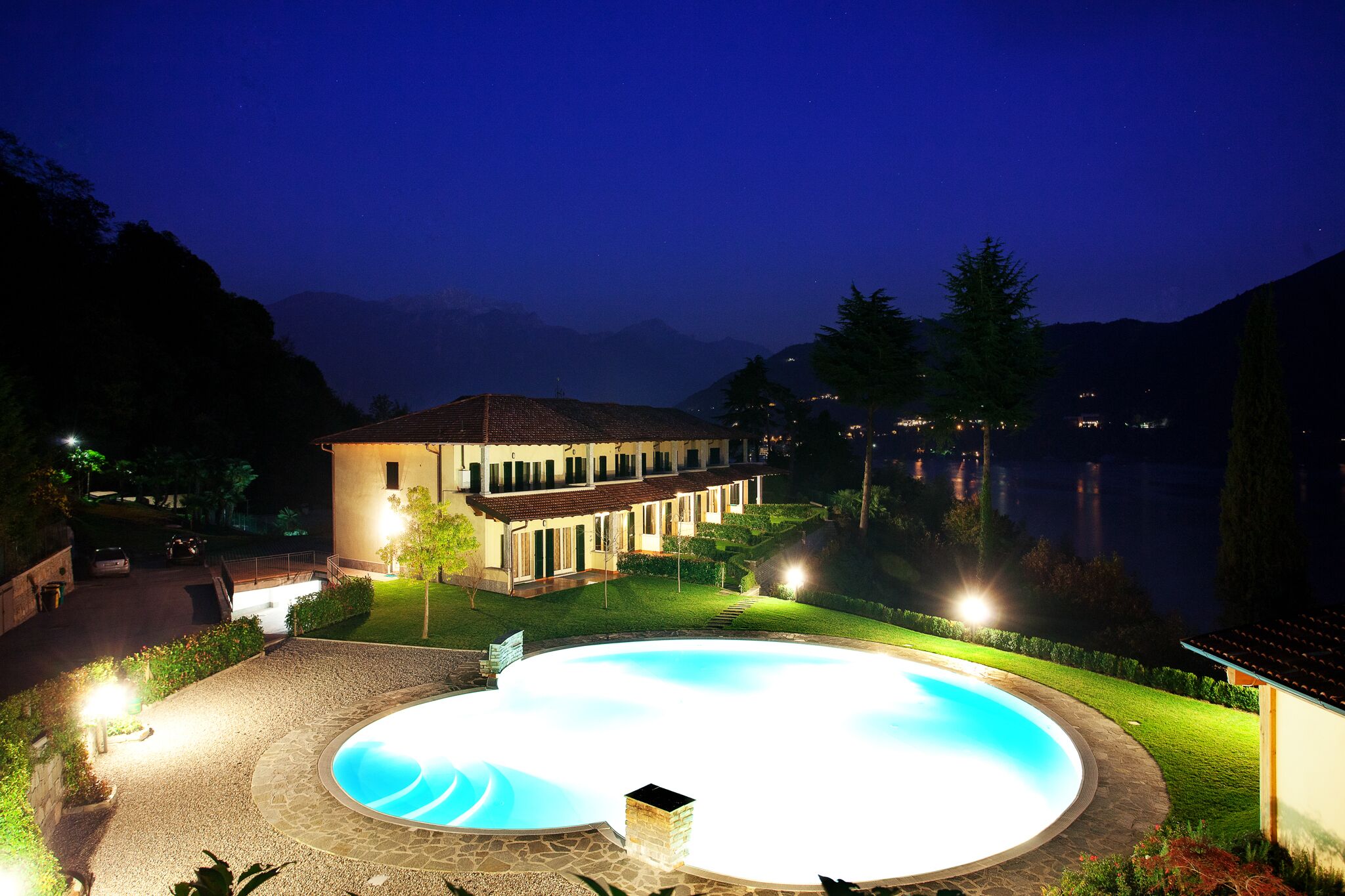 A well-lit swimming pool area with a house in the background.