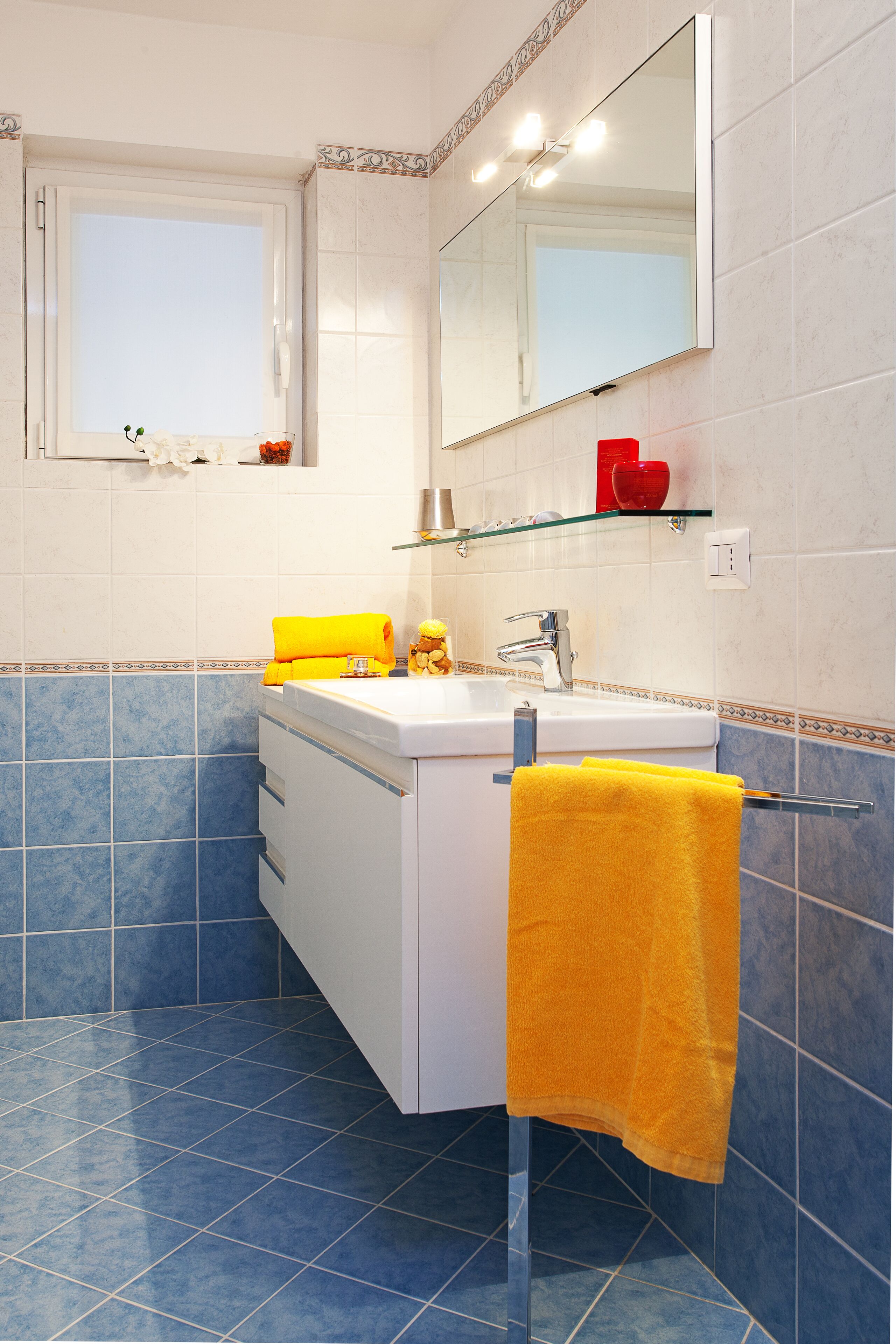 Une salle de bain avec un lavabo blanc, un miroir et une fenêtre.