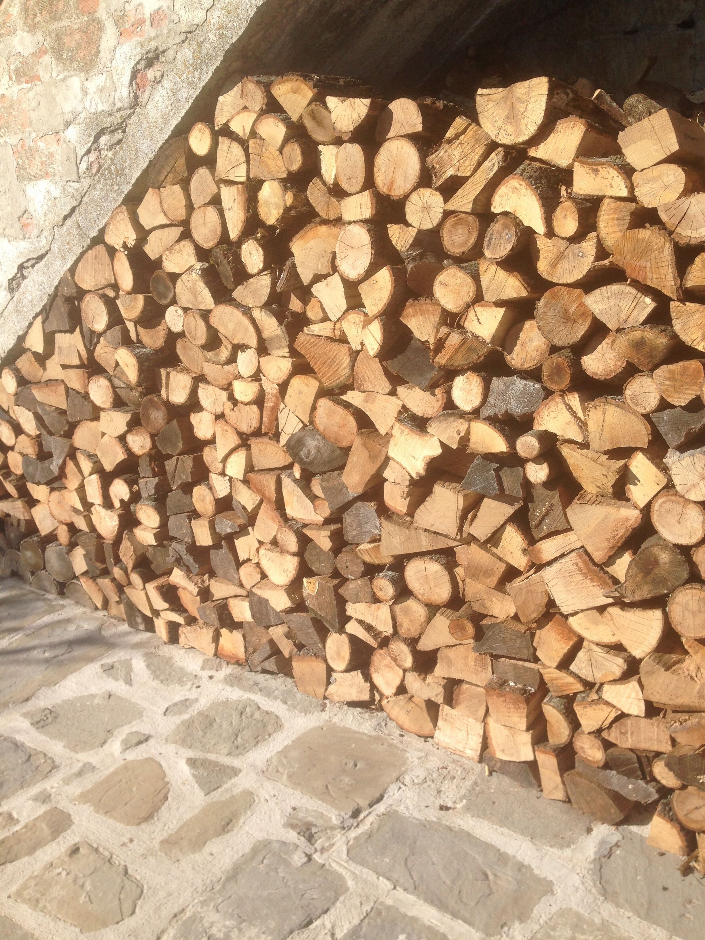 Een stapel hout tegen een stenen muur.
