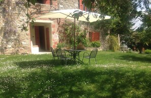 Une terrasse extérieure avec une table et des chaises, entourée d’un mur de pierre et de verdure.