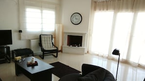 A living room with a sofa, a coffee table, a chair, a fireplace, and a clock on the wall. - Luxury Apartment Thermaikos (Thermaikos)