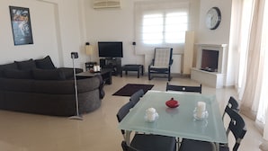 A modern living room with a sofa, TV, fireplace, and dining area with chairs and a table. - Luxury Apartment Thermaikos (Thermaikos)