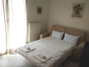 Uma cama bem arrumada com roupa de cama branca, um radiador e um quadro na parede.
